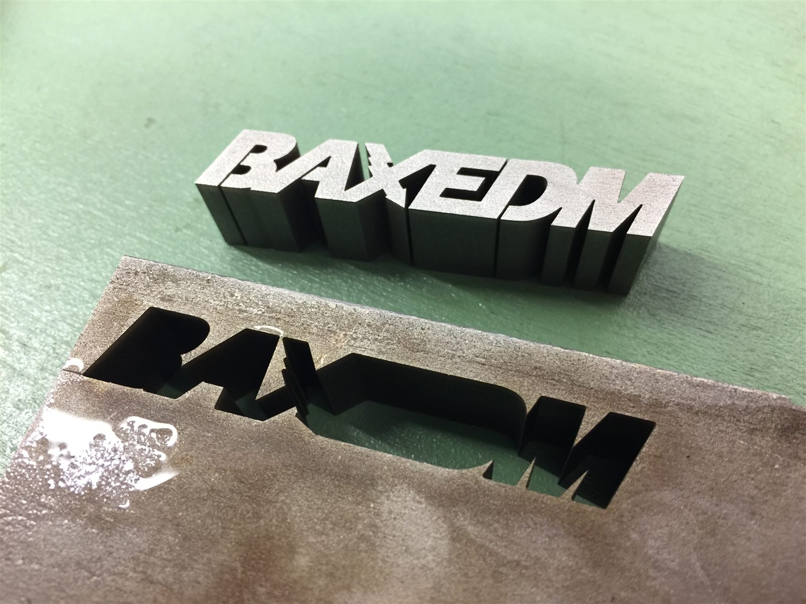 BAXEDM letters cut from a metal plate